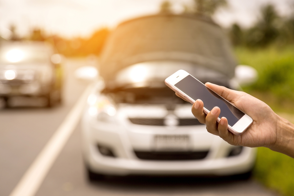 a person on their phone standing in front of a car to denote car maintenance checks