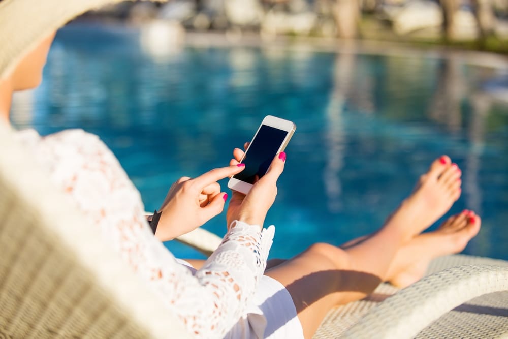 someone on their phone on a beach to denote a data roaming bill warning for holidaymakers