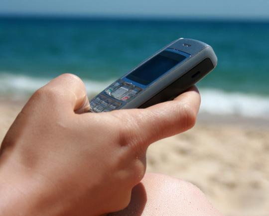someone on their phone on a beach to denote a data roaming bill warning for holidaymakers